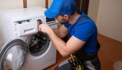 Worker repairing washing machine in laundry room.
